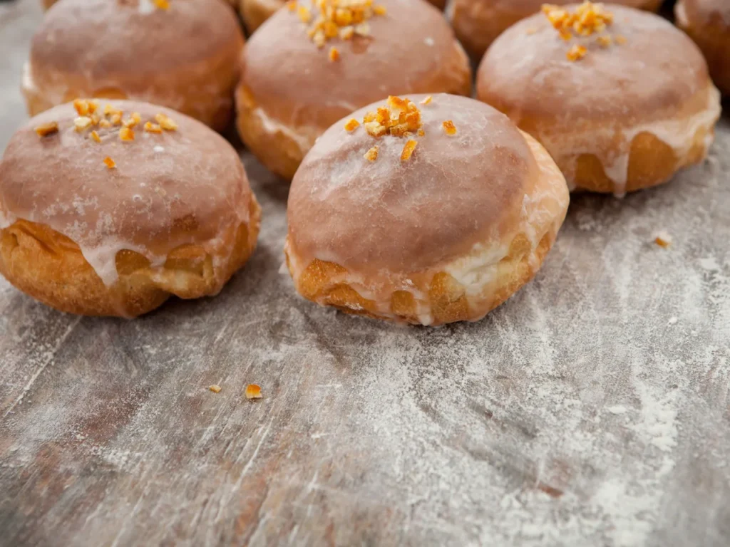 Pączki w lukrze ze skórką pomarańczową, leżące na drewnianej desce posypanej mąką